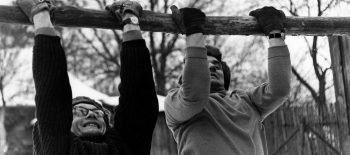 Кадр з фільму: двоє чоловіків у шапках і свертах підтягуються на колоді вгору