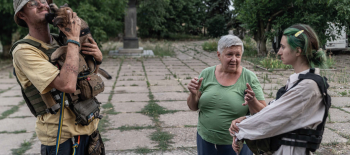Чоловік у касці тримає на руках пса, навпроти нього стоїть старша жінка і дівчина-підлітка