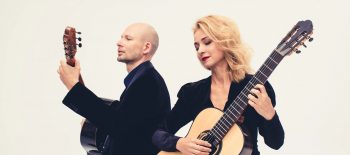 Na fotografii je kytarové duo Ewa Jabłczyńska a Dariusz Kupiński, sedí a v rukou drží kytary. Oba sedí a za nimi je čistě bílé pozadí.