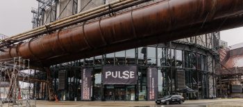 Na fotografii je multifunkční hala Gong, která vznikla vestavbou do objektu bývalého průmyslového plynojemu. Nad vchodem je název akce: PULSE