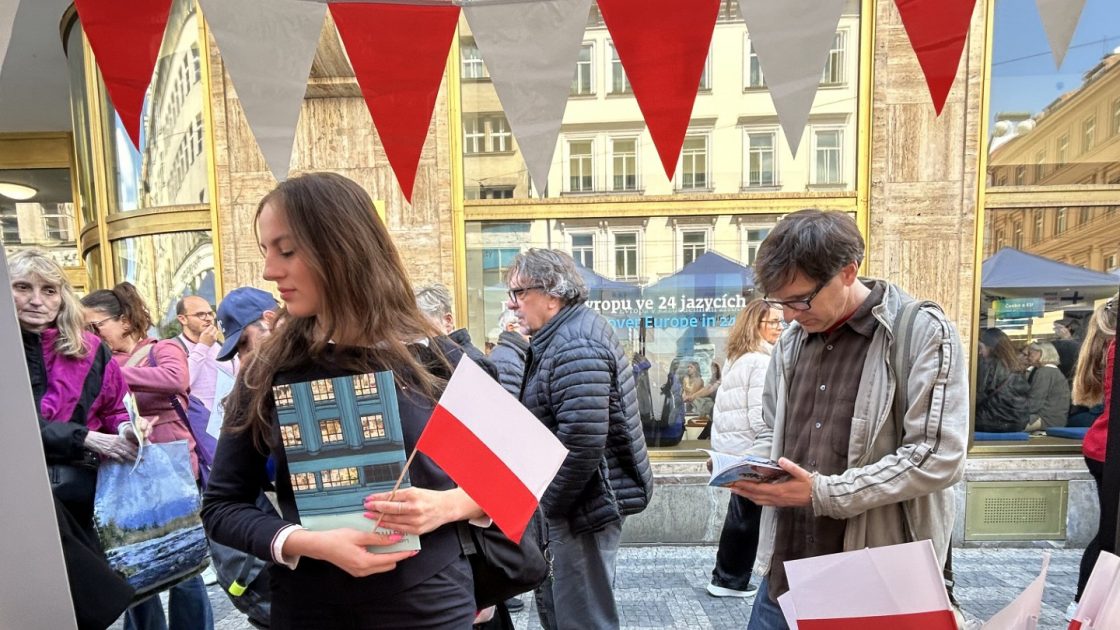 Polský stánek na Dni Evropy v roce 2025 - obsahuje polské vlaječky, letáky, sladkosti a propagační předměty, u stánku stojí dvě osoby.