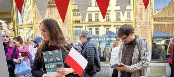 Polský stánek na Dni Evropy v roce 2025 - obsahuje polské vlaječky, letáky, sladkosti a propagační předměty, u stánku stojí dvě osoby.