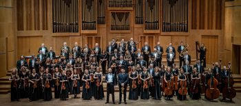 Na fotografii je symfonický orchestr z města Opolí. Skupinová fotografie velkého orchestru je v interiéru koncertní síně, v pozadí jeviště jsou vidět píšťaly varhan.