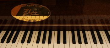 Na fotografii je klaviatura koncertního křídla. Nad klávesami je připevněna oválná tabulka zlaté barvy s podpisem Chopin.
