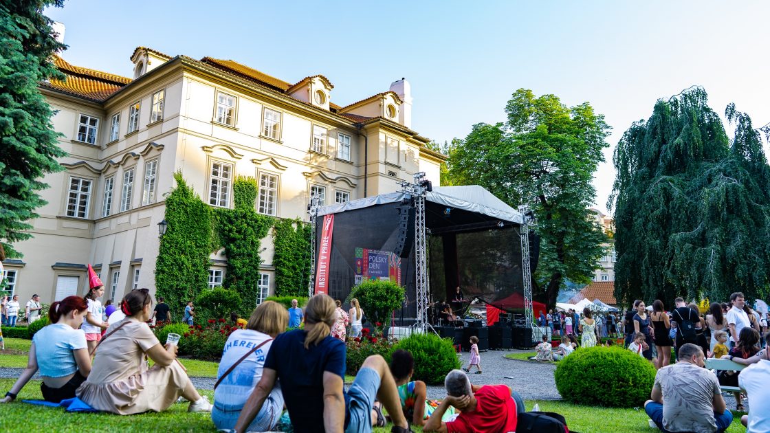 Na fotografii je barokní budova Fürstenberského paláce a v jeho zahradě je umístěno pódium, před kterým sedí na trávě lidé