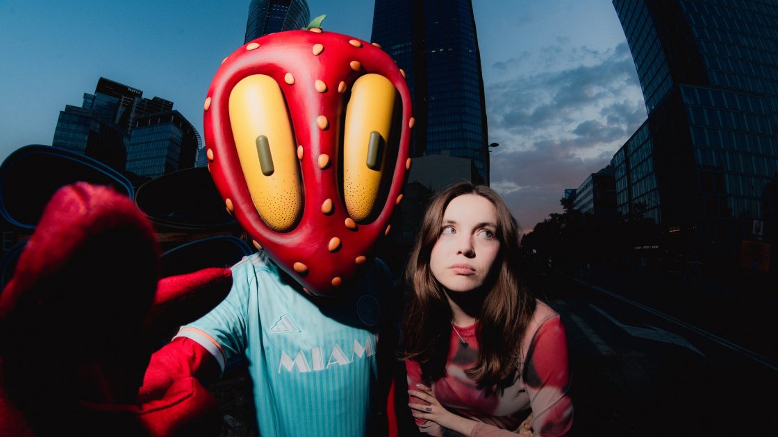 Na fotografii je na pozadí města zpěvačka Dominika Płonka a hudebník DJ BLIK, který má na hlavě nasazenou masku ve tvaru obří jahody.