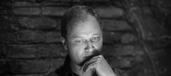 Na černobílé fotografii je muž středního věku, básník Krzysztof Siwczyk. Má zamyšlený pohled, dívá se na zem a rukou se dotýká brady.