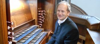 Der Organist und Pianist Michał Dąbrowski sitzt lächelnd neben der Orgel.